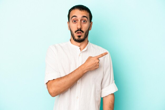 Jeune homme de race blanche isolé sur fond bleu pointant vers le côté