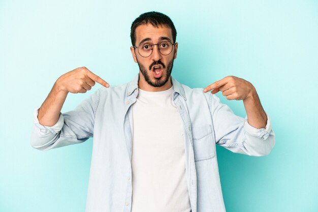 Jeune homme de race blanche isolé sur fond bleu pointe vers le bas avec les doigts, sentiment positif.