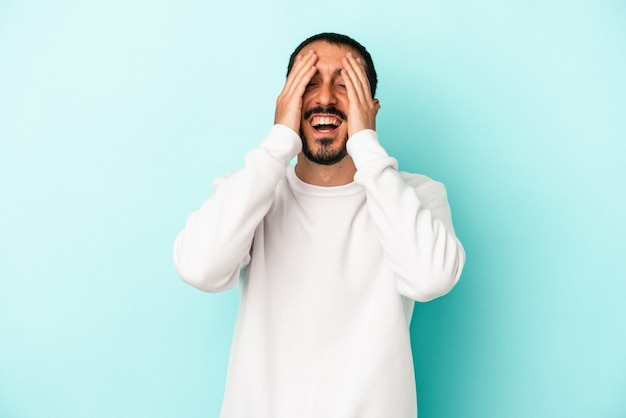 Jeune homme de race blanche isolé sur fond bleu rit joyeusement en gardant les mains sur la tête. Notion de bonheur.