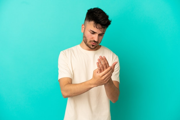 Jeune homme de race blanche isolé sur fond bleu souffrant de douleurs dans les mains