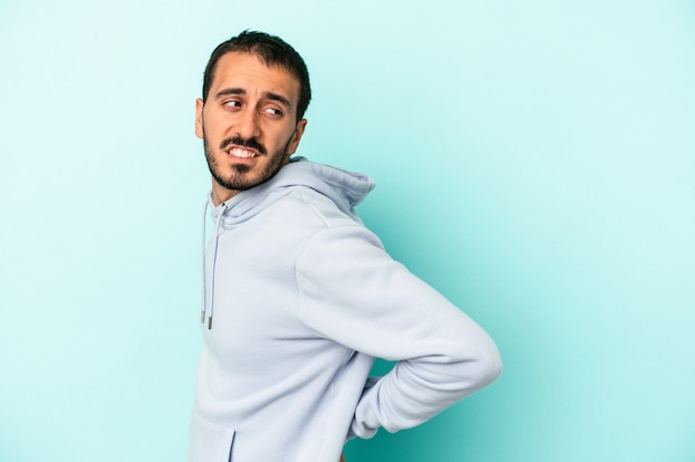 Jeune homme de race blanche isolé sur fond bleu souffrant d'un mal de dos.