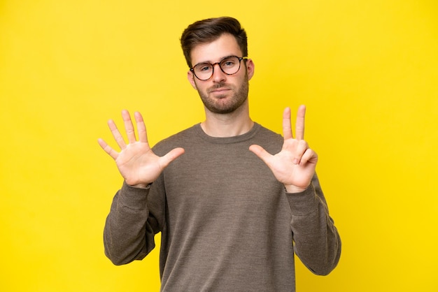 Jeune homme de race blanche isolé sur fond jaune comptant huit avec les doigts