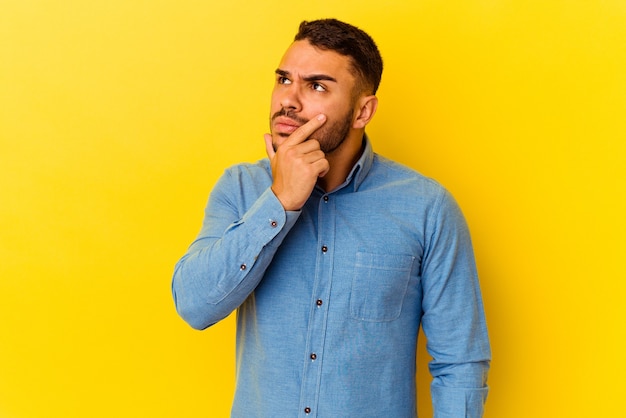 Jeune homme de race blanche isolé sur fond jaune contemplant, planifiant une stratégie, réfléchissant à la manière d'une entreprise.