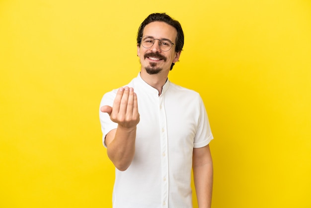 Jeune homme de race blanche isolé sur fond jaune invitant à venir avec la main. Heureux que tu sois venu