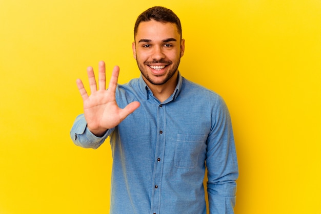 Jeune homme de race blanche isolé sur fond jaune souriant joyeux montrant le numéro cinq avec les doigts.