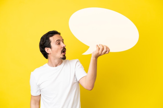 Jeune homme de race blanche isolé sur fond jaune tenant une bulle de dialogue vide