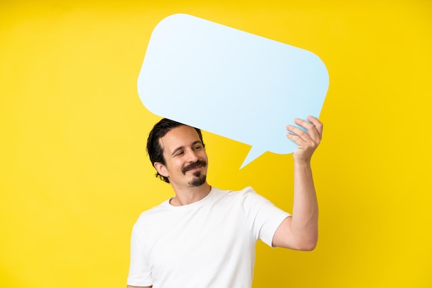 Jeune homme de race blanche isolé sur fond jaune tenant une bulle de dialogue vide