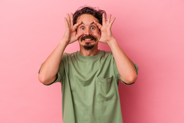 Jeune homme de race blanche isolé sur fond rose en gardant les yeux ouverts pour trouver une opportunité de réussite.