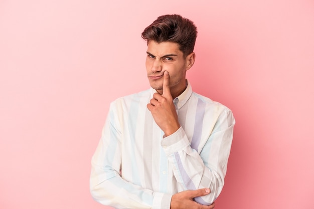 Jeune homme de race blanche isolé sur fond rose malheureux à la recherche à huis clos avec une expression sarcastique.