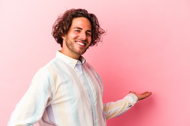 Jeune homme de race blanche isolé sur fond rose montrant une expression de bienvenue.