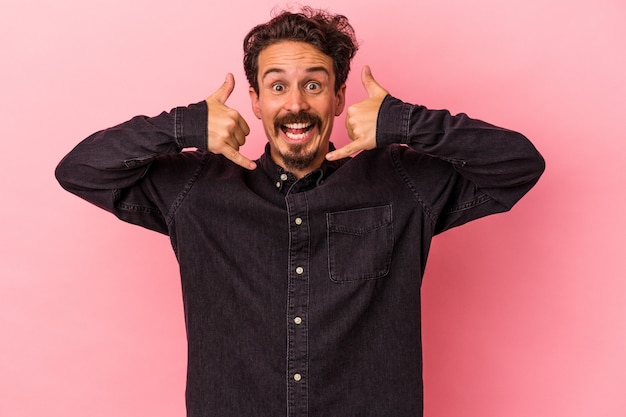 Jeune homme de race blanche isolé sur fond rose montrant un geste d'appel de téléphone portable avec les doigts.