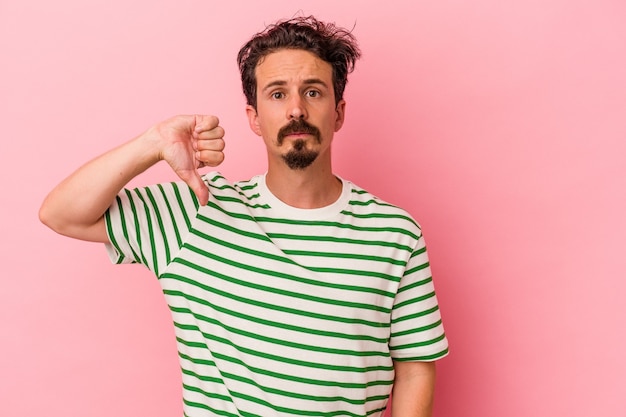 Jeune homme de race blanche isolé sur fond rose montrant un geste d'aversion, les pouces vers le bas. Notion de désaccord.