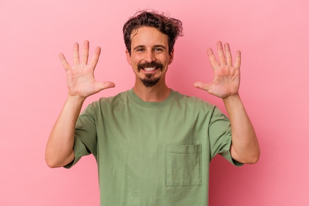 Jeune homme de race blanche isolé sur fond rose montrant le numéro dix avec les mains.