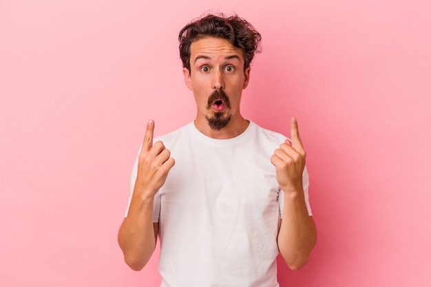 Jeune homme de race blanche isolé sur fond rose pointant vers le haut avec la bouche ouverte.