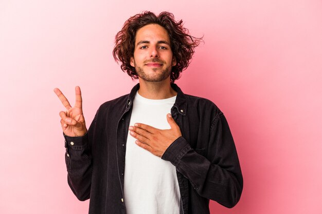 Jeune homme de race blanche isolé sur fond rose prêtant serment, mettant la main sur la poitrine.