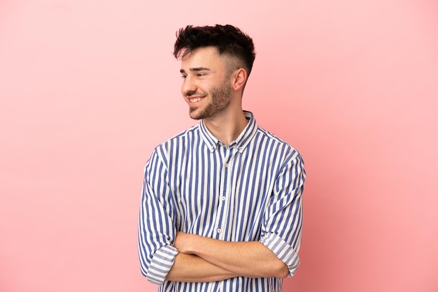 Jeune homme de race blanche isolé sur fond rose regardant sur le côté et souriant