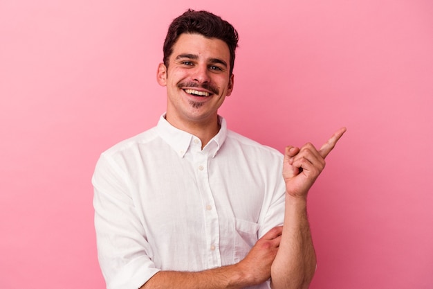 Jeune homme de race blanche isolé sur fond rose souriant joyeusement pointant avec l'index loin.