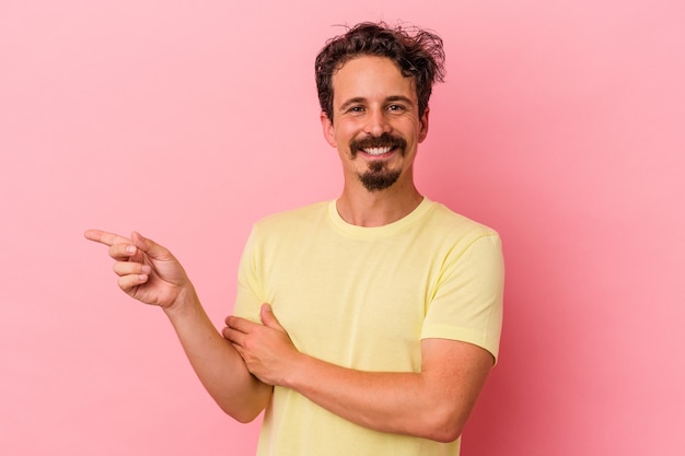 Jeune homme de race blanche isolé sur fond rose souriant joyeusement pointant avec l'index loin.