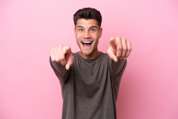 Jeune homme de race blanche isolé sur fond rose surpris et pointant vers l'avant