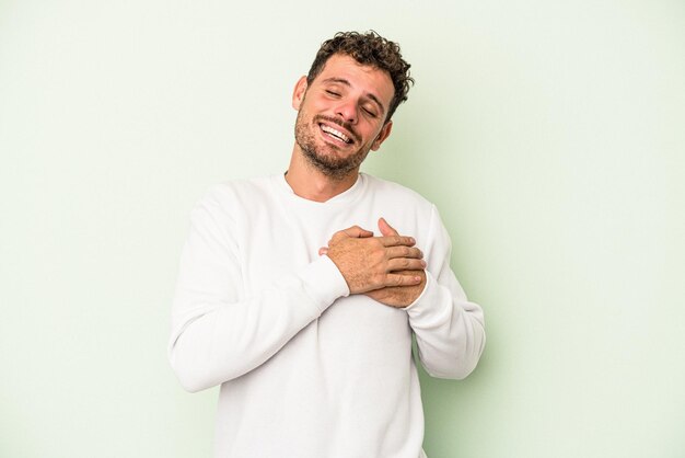 Jeune Homme De Race Blanche Isolé Sur Fond Vert A Une Expression Amicale, Appuyant La Paume Sur La Poitrine. Notion D'amour.