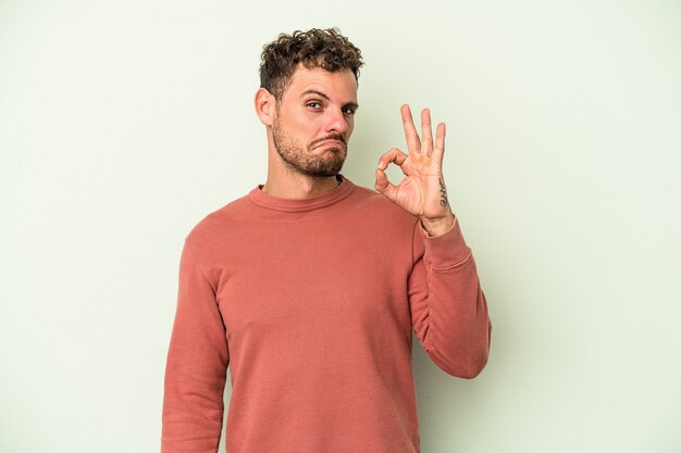 Jeune homme de race blanche isolé sur fond vert fait un clin d'œil et tient un geste correct avec la main.