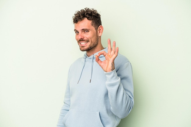 Jeune homme de race blanche isolé sur fond vert fait un clin d'œil et tient un geste correct avec la main.