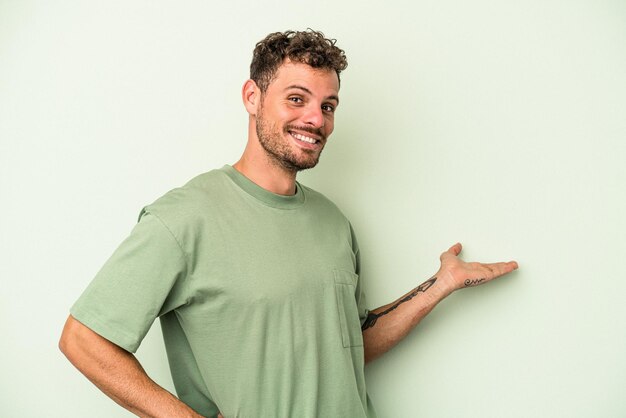 Jeune homme de race blanche isolé sur fond vert montrant une expression de bienvenue.