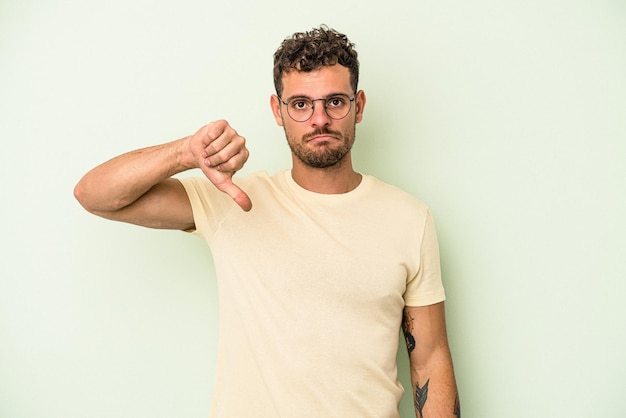 Jeune homme de race blanche isolé sur fond vert montrant un geste d'aversion, les pouces vers le bas. Notion de désaccord.