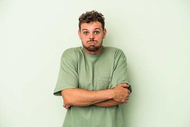 Jeune homme de race blanche isolé sur fond vert souffle les joues, a une expression fatiguée. Concept d'expression faciale.