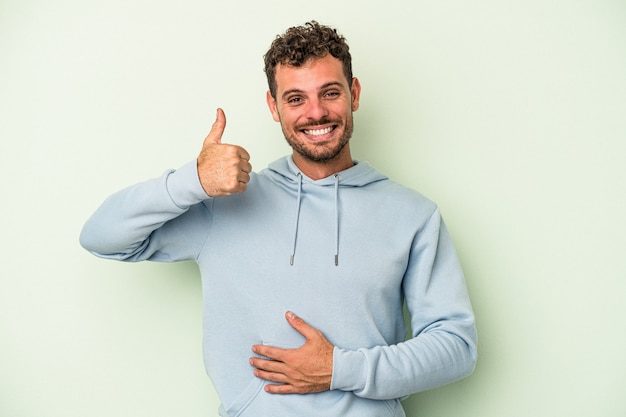 Un jeune homme de race blanche isolé sur fond vert touche le ventre, sourit doucement, mange et satisfait le concept.