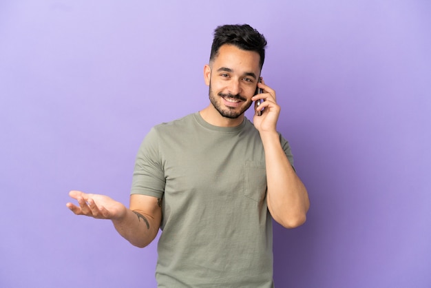 Jeune homme de race blanche isolé sur fond violet en gardant une conversation avec le téléphone portable avec quelqu'un