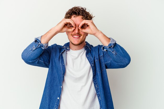 Jeune homme de race blanche isolé sur un mur blanc montrant un signe correct sur les yeux