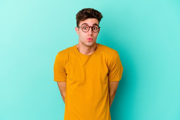 Jeune homme de race blanche isolé sur un mur bleu hausse les épaules et les yeux ouverts confus