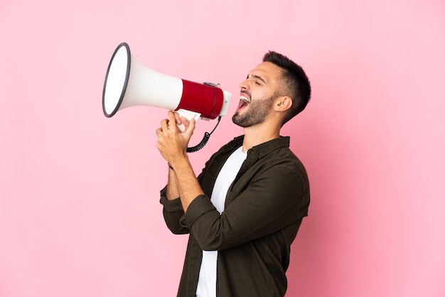 Jeune homme de race blanche isolé sur un mur rose en criant à travers un mégaphone pour annoncer quelque chose en position latérale