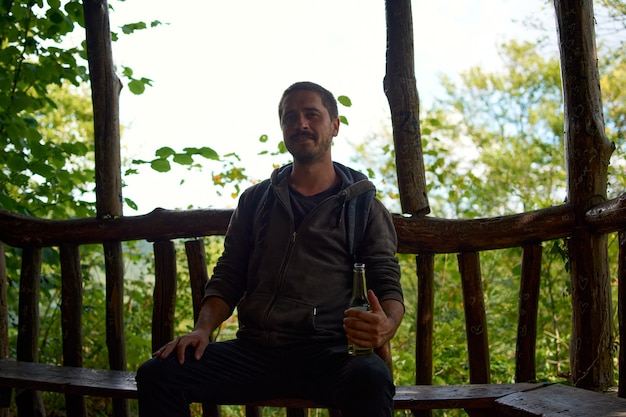 Un jeune homme de race blanche joyeux buvant de la bière dans un parc pendant la journée