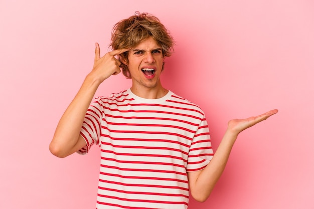 Jeune homme de race blanche avec maquillage isolé sur fond rose montrant un geste de déception avec l'index.