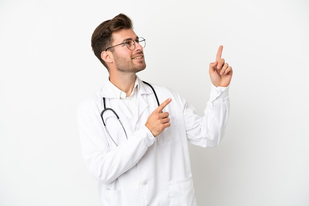 Jeune homme de race blanche médecin sur isolé sur fond blanc portant une robe de médecin et pointant vers le haut