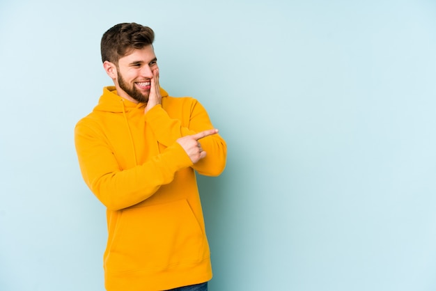 Jeune homme de race blanche sur le mur bleu en disant un potin, pointant vers le côté signaler quelque chose.