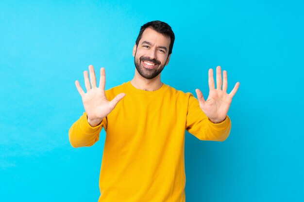 Jeune homme de race blanche sur mur bleu isolé comptant dix avec les doigts