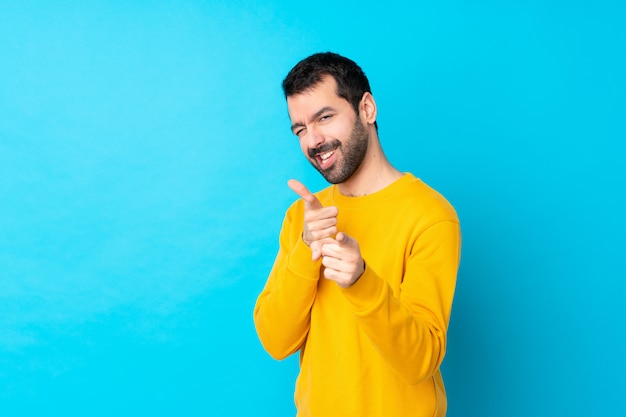 Jeune homme de race blanche sur mur bleu isolé pointant vers l'avant et souriant