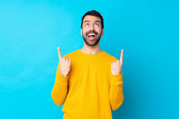 Jeune homme de race blanche sur mur bleu isolé surpris et pointant vers le haut