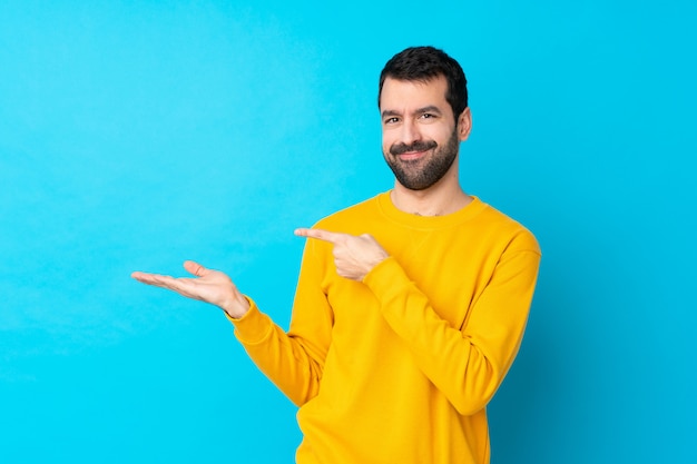 Jeune homme de race blanche sur mur bleu isolé tenant copyspace imaginaire sur la paume pour insérer une annonce