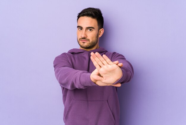 Jeune homme de race blanche sur mur violet debout avec la main tendue montrant le panneau d'arrêt