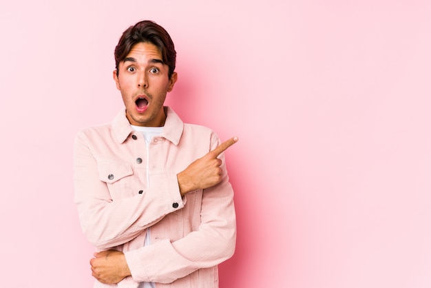 Jeune homme de race blanche posant dans un mur rose isolé pointant vers le côté