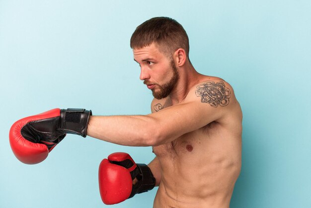 Jeune homme de race blanche pratiquant la boxe isolé sur fond bleu