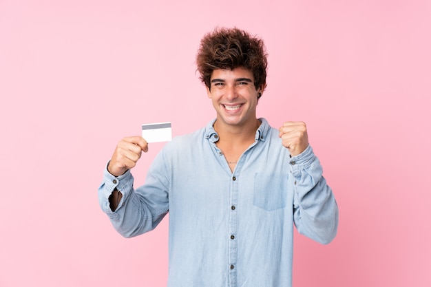 Jeune homme de race blanche sur rose isolé tenant une carte de crédit