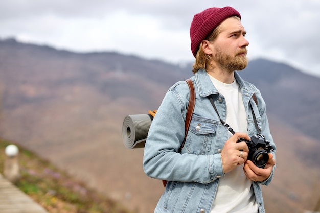 Jeune homme de race blanche avec sac à dos et appareil photo marche vers la montagne lointaine