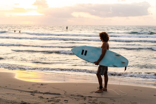 Jeune homme de race blanche se lève tôt pour faire du surf au lever du soleil