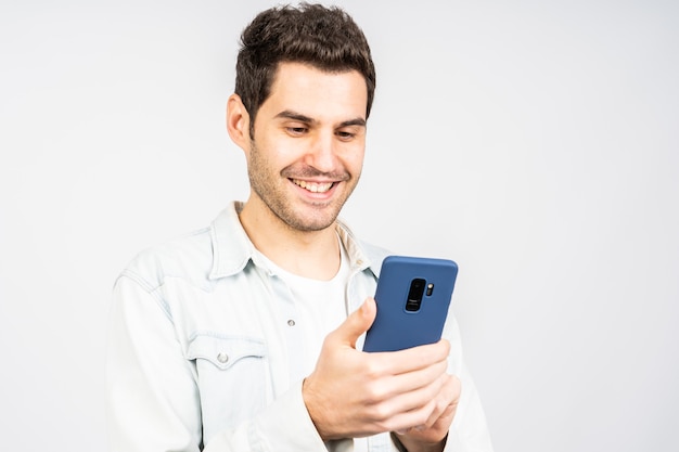 Jeune homme de race blanche souriant tout en travaillant sur le mobil contre un mur blanc