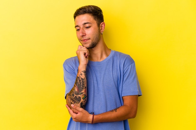 Jeune homme de race blanche avec des tatouages isolés sur fond jaune regardant de côté avec une expression douteuse et sceptique.